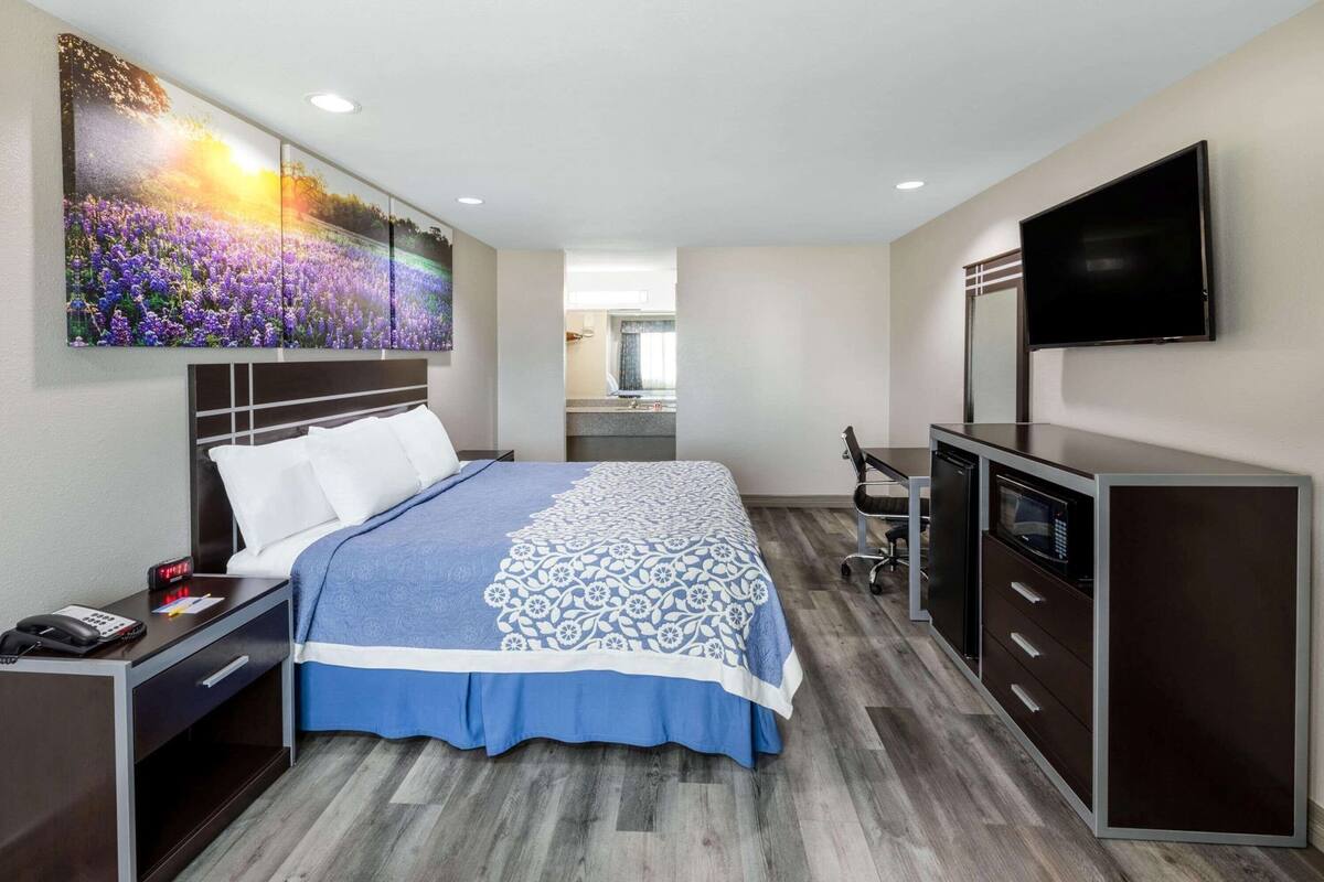 A hotel room with a bed, a desk, a TV, and a large painting on the wall.