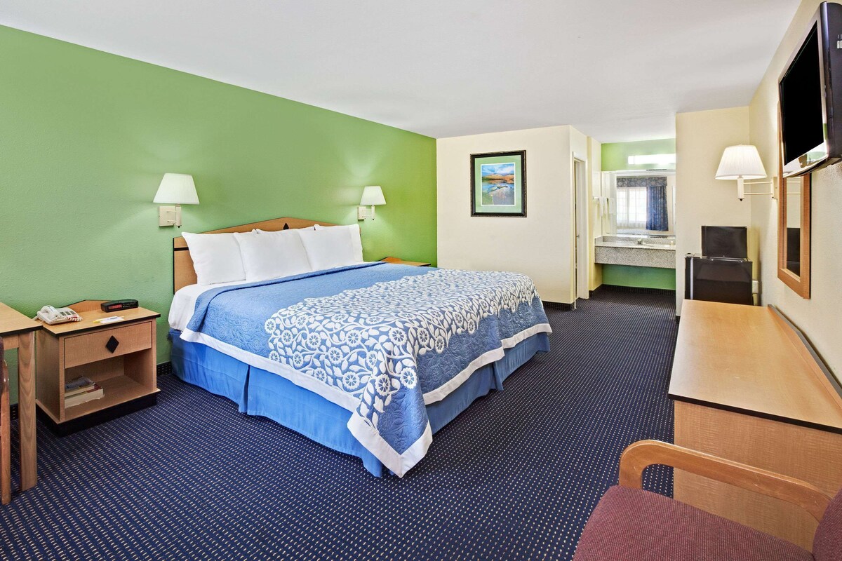A hotel room with a bed, bedside tables, a desk, a chair, a television, and a bathroom visible through an open door.