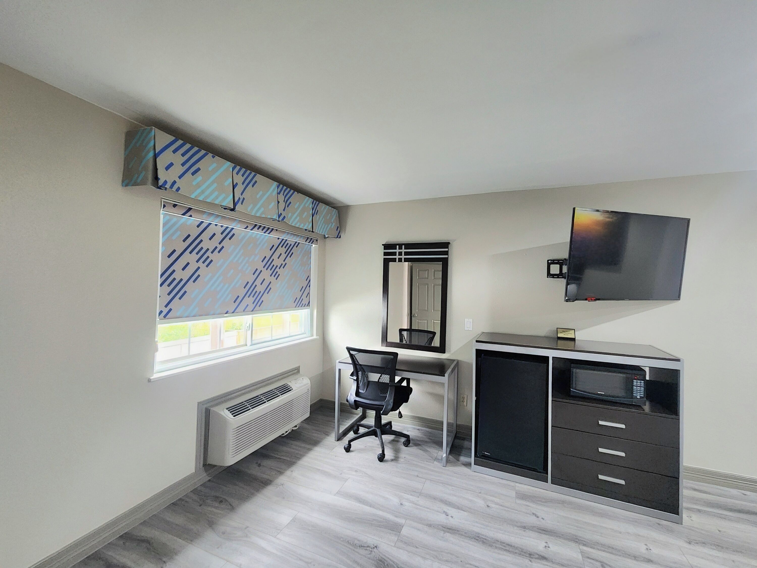 A room with a desk, chair, TV, and built-in storage.