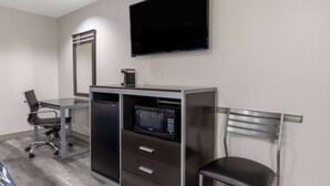 Une chambre d’hôtel moderne équipée d’un bureau, d’une chaise, d’un four à micro-ondes encastré et d’un téléviseur à écran plat fixé au mur.