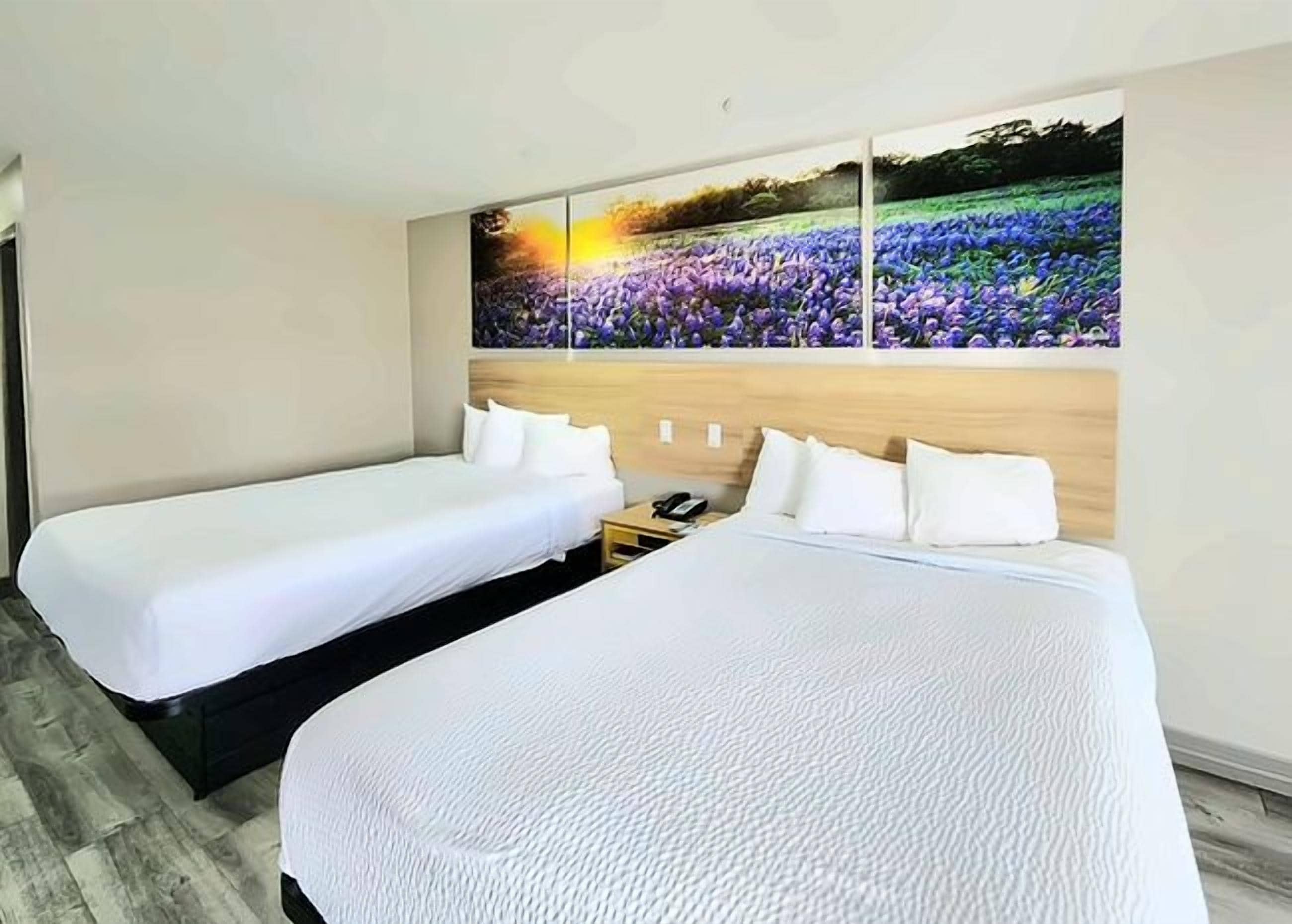 A hotel room with two beds, a wooden headboard, and a large floral artwork on the wall.