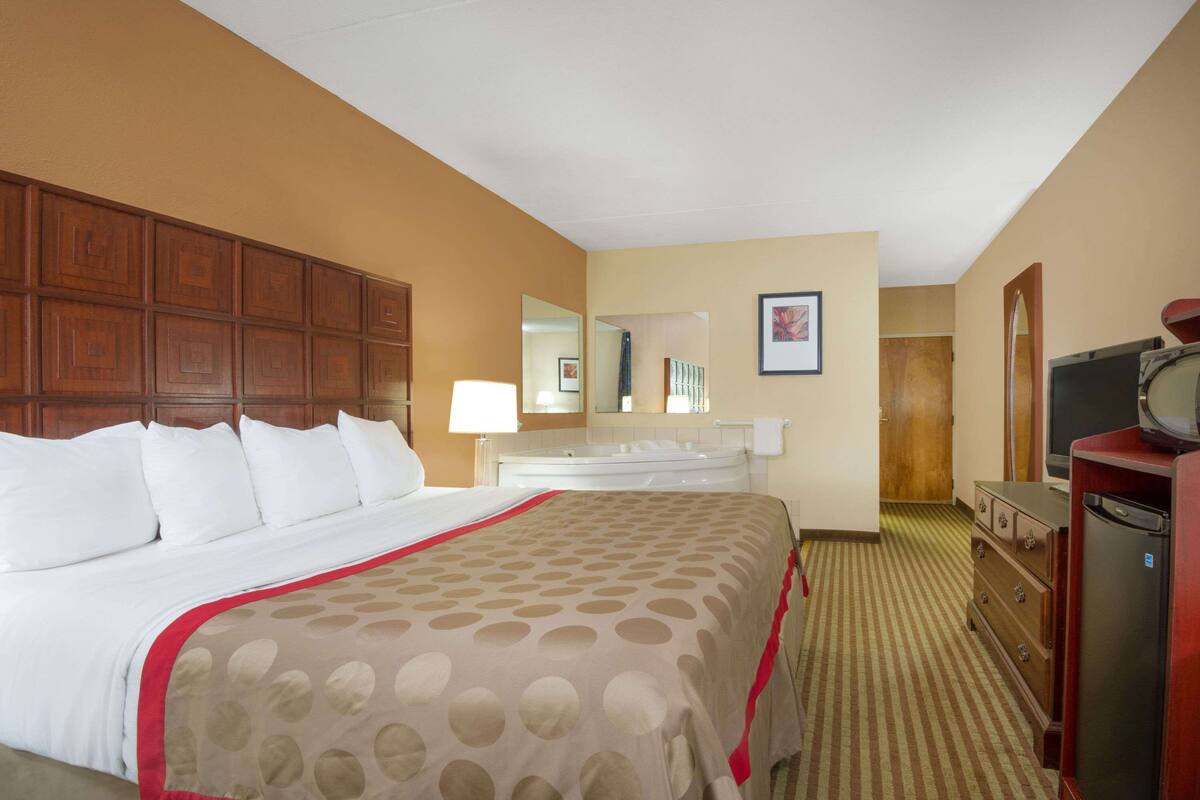 A hotel room with a large bed, a dresser, a television, and a bathroom visible in the background.