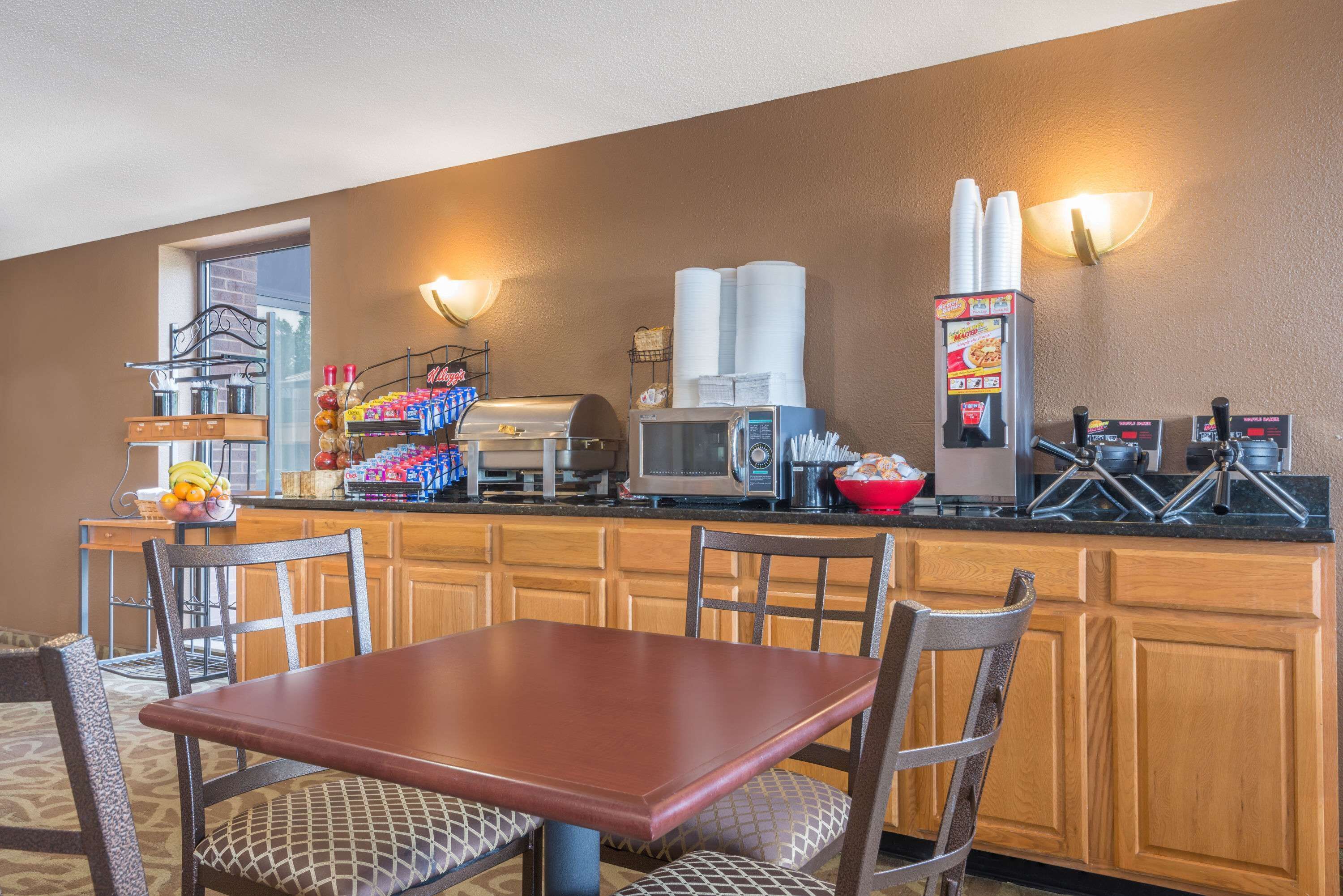 A hotel kitchenette with a microwave, toaster, and coffee maker. There is a dining table with chairs and a fruit bowl on the counter.