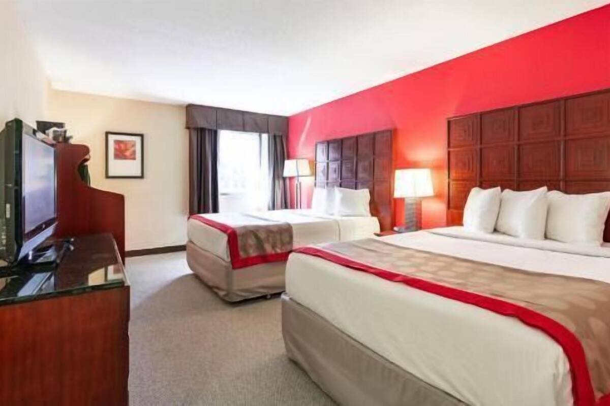 A hotel room with two beds, a desk, a television, and a window with curtains.