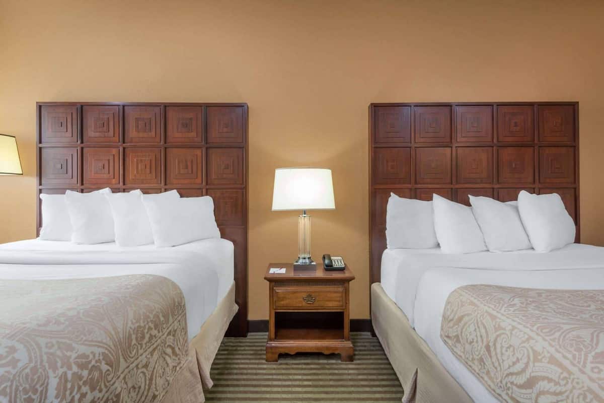 A hotel room with two beds, a nightstand with a lamp, and a wooden headboard.