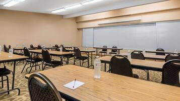 Une salle de conférence dotée de plusieurs tables et chaises, équipée de bouteilles d’eau et de stylos, et un tableau blanc fixé au mur.