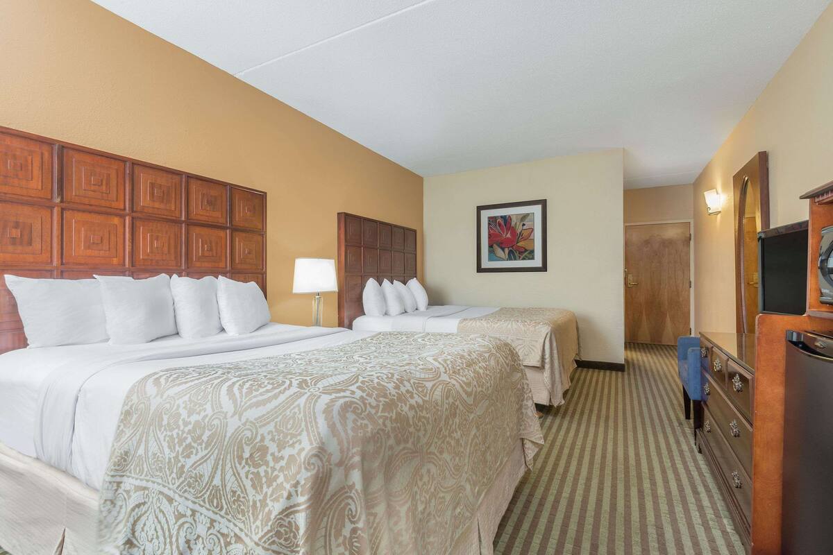 A hotel room with two beds, a wooden headboard, a painting, a dresser, and a television.
