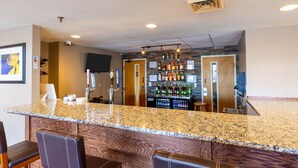 A bar area with granite countertops, leather bar stools, and a variety of liquor bottles. - Ramada by Wyndham Columbus North (Columbus)