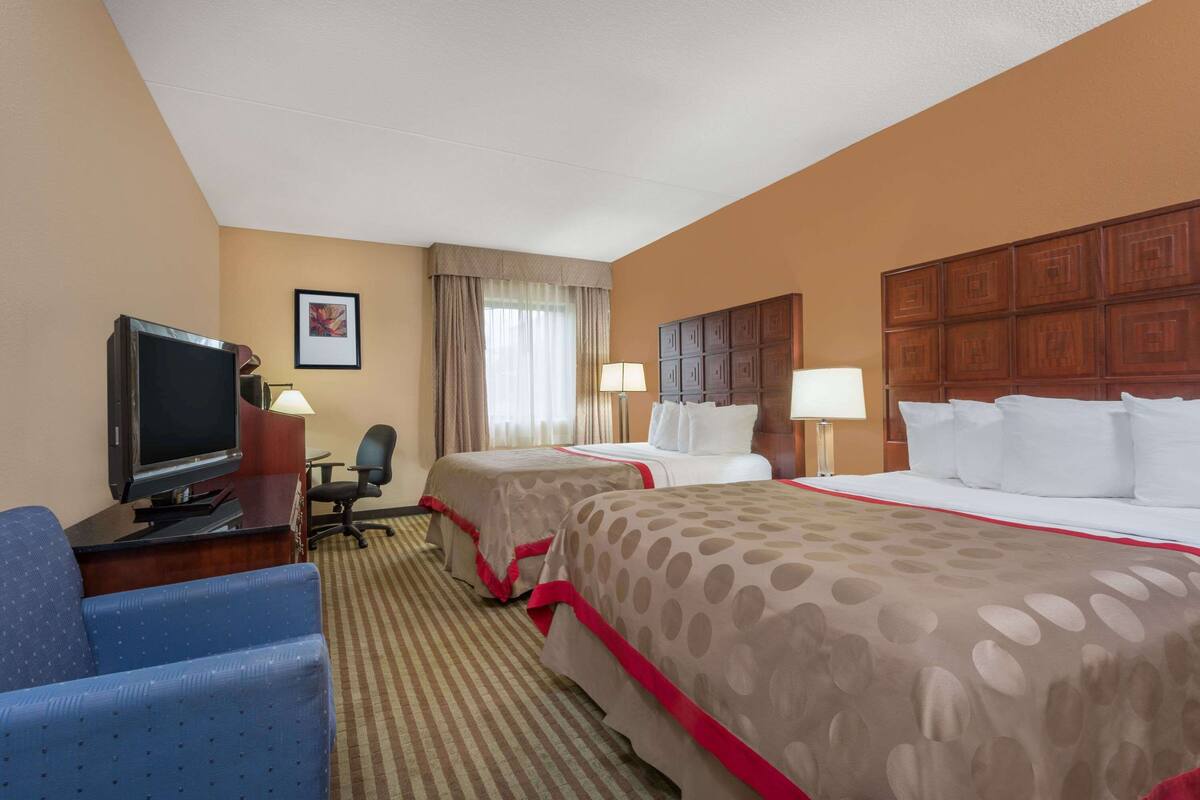 A hotel room with two beds, a desk with a television, a chair, and a lamp.
