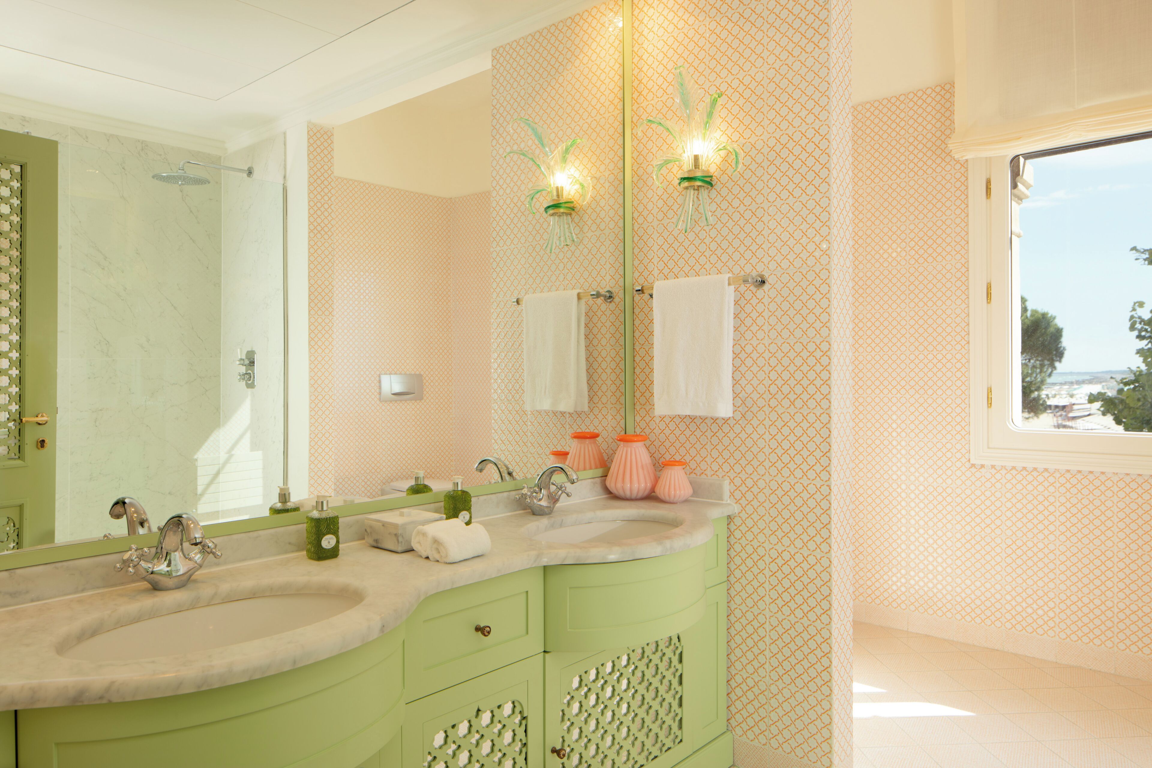 Un baño con tocador verde, un espejo grande, dos luces empotradas en la pared y una ventana con vistas.