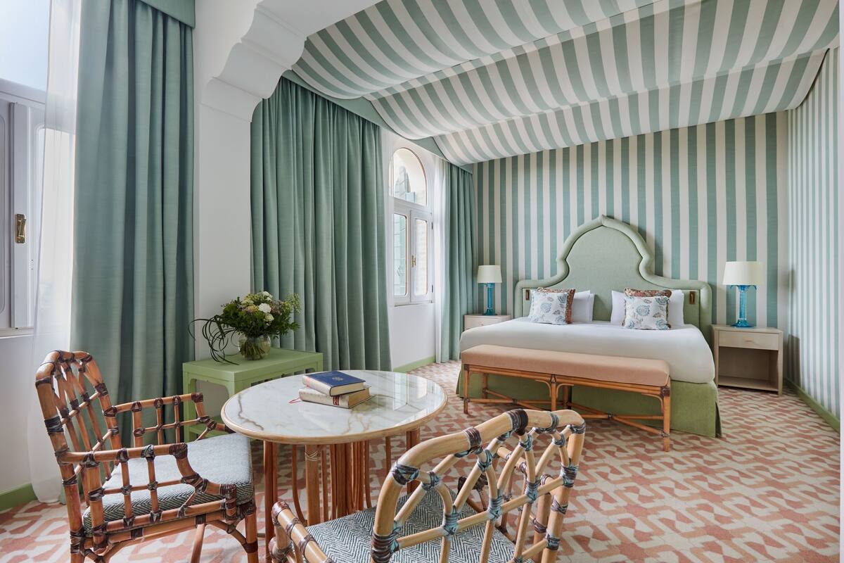 A hotel room with a large bed, two nightstands, a round table, and two wicker chairs.