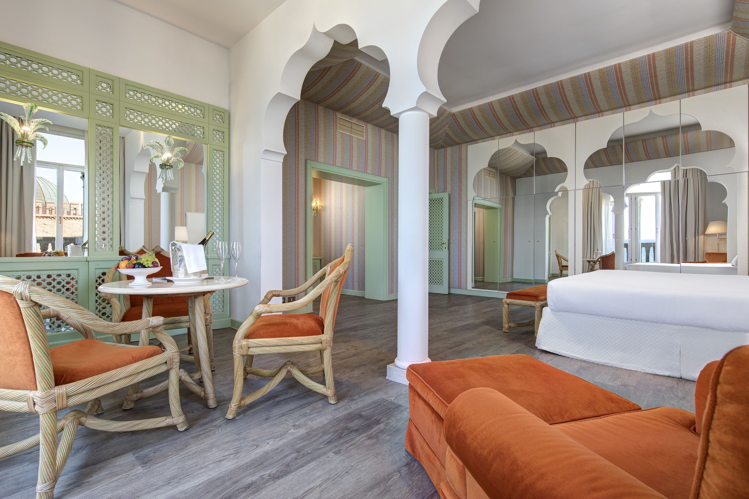 A hotel room with a dining area, a bed, and a large mirror.