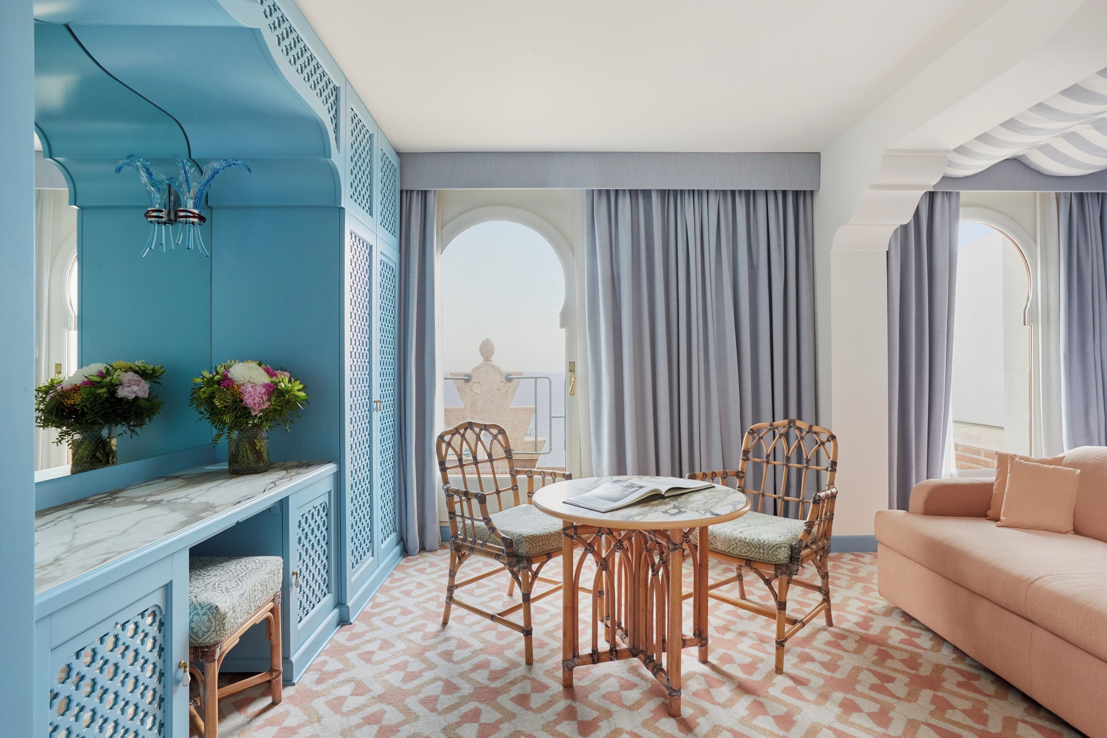 Une pièce avec un mur d’accent bleu, une table ronde avec des chaises, un canapé et une vue par une fenêtre avec des rideaux.
