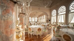 A grand dining hall with ornate chandeliers, marble columns, and classical statues. Tables are set with white tablecloths and green chairs. - Hotel Excelsior Venice (Venice)