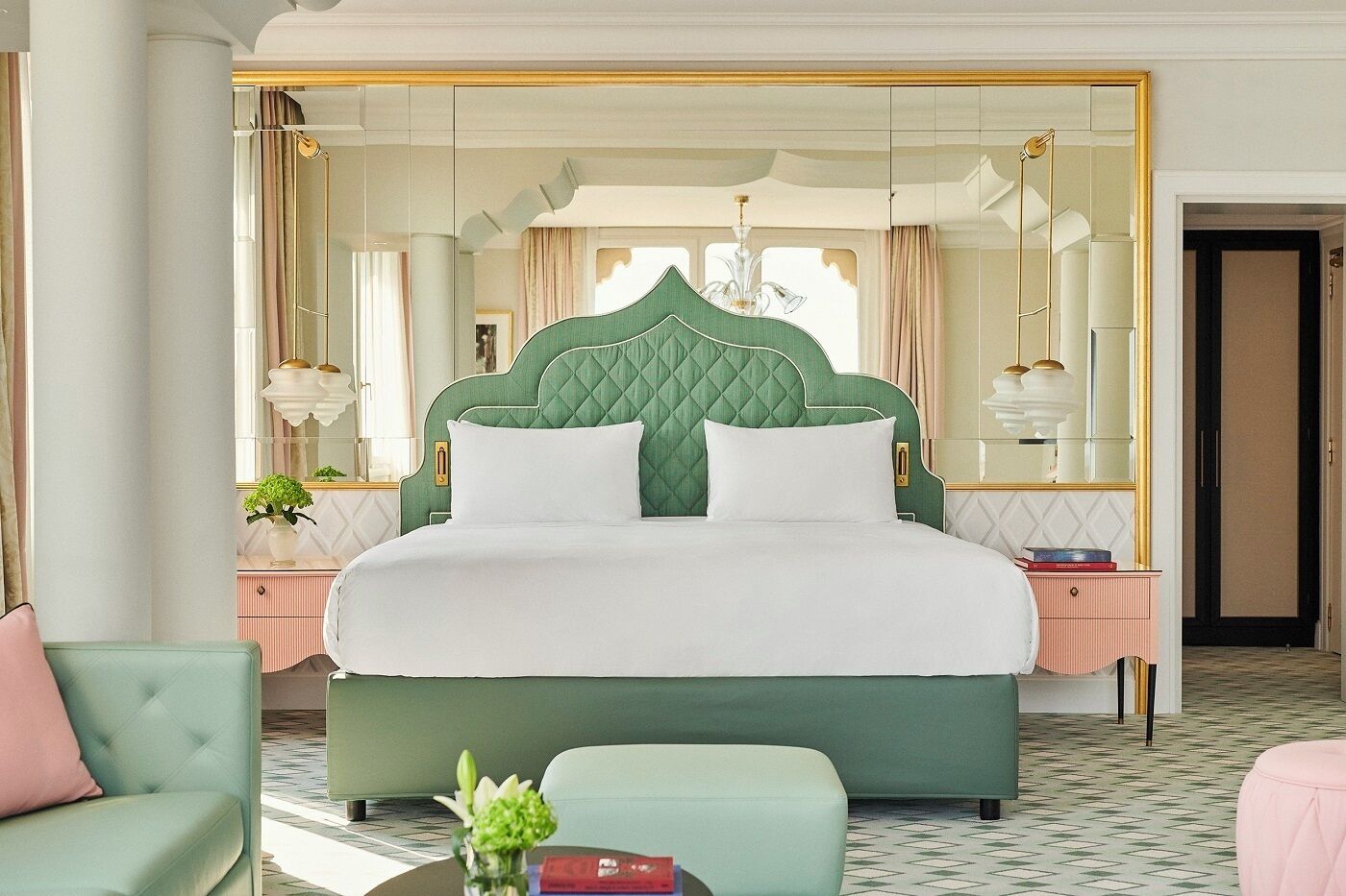 Een ruime slaapkamer met een groot bed, een groen bekleden hoofdeinde en een grote spiegel boven het bed.