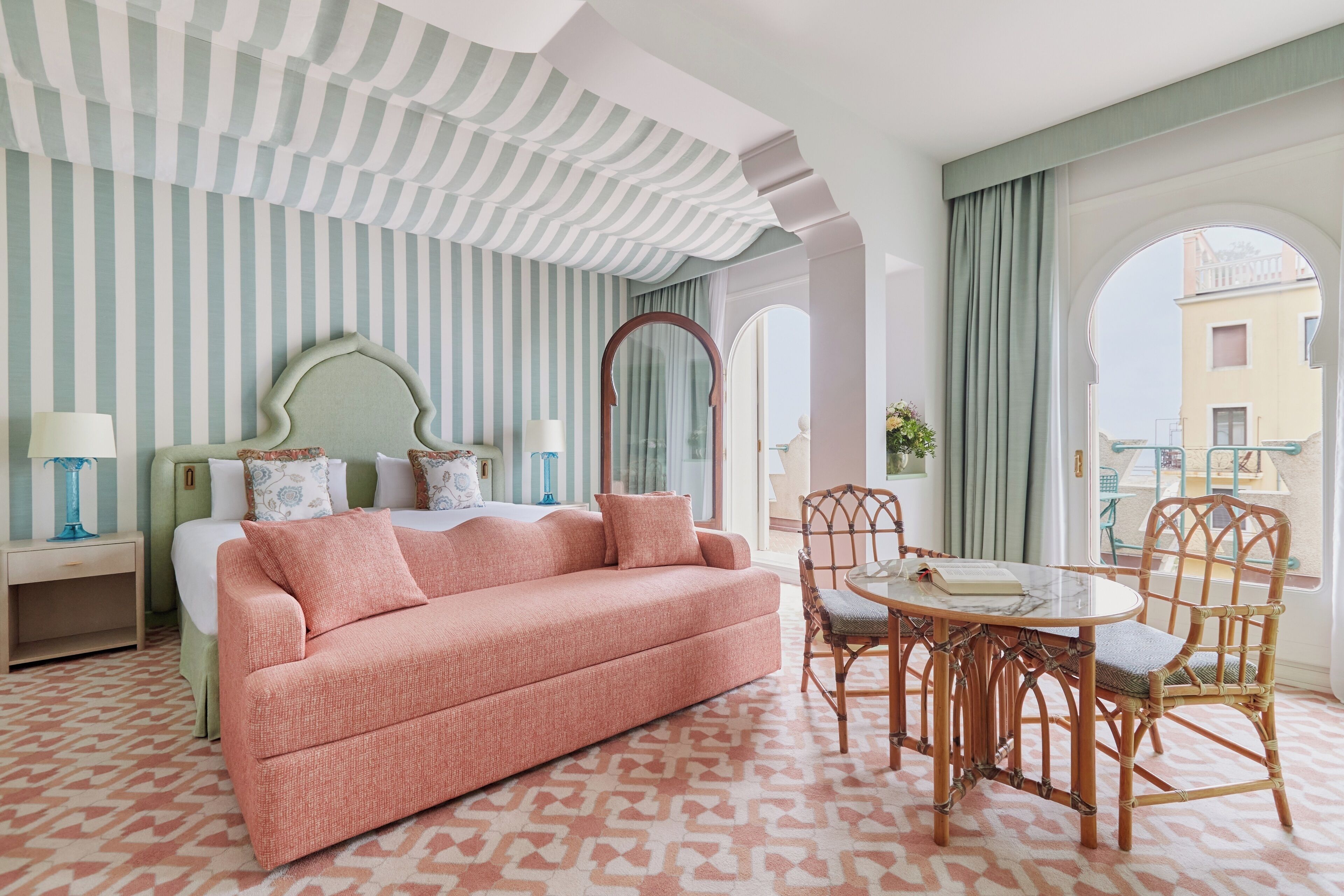 A hotel room with a bed, a pink sofa, a round table with chairs, and striped wallpaper.