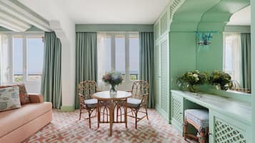 A room with a sofa, a round table with chairs, a console table with plants, and a view through large windows.
