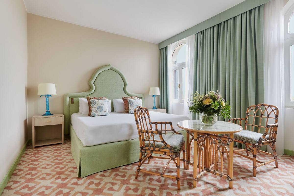 A hotel room with a bed, two nightstands, a round table with chairs, and a window with curtains.