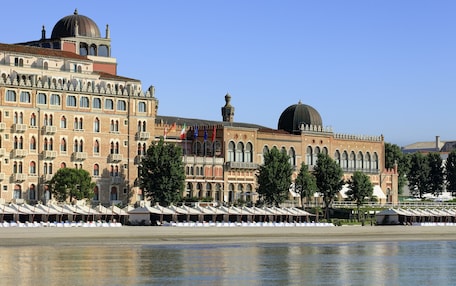 A historic building with arched windows and a dome, adjacent to a waterfront with rows of white umbrellas.