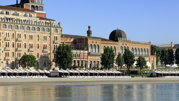 A historic building with arched windows and a dome, adjacent to a waterfront with rows of white umbrellas. - Hotel Excelsior Venice (Venice)