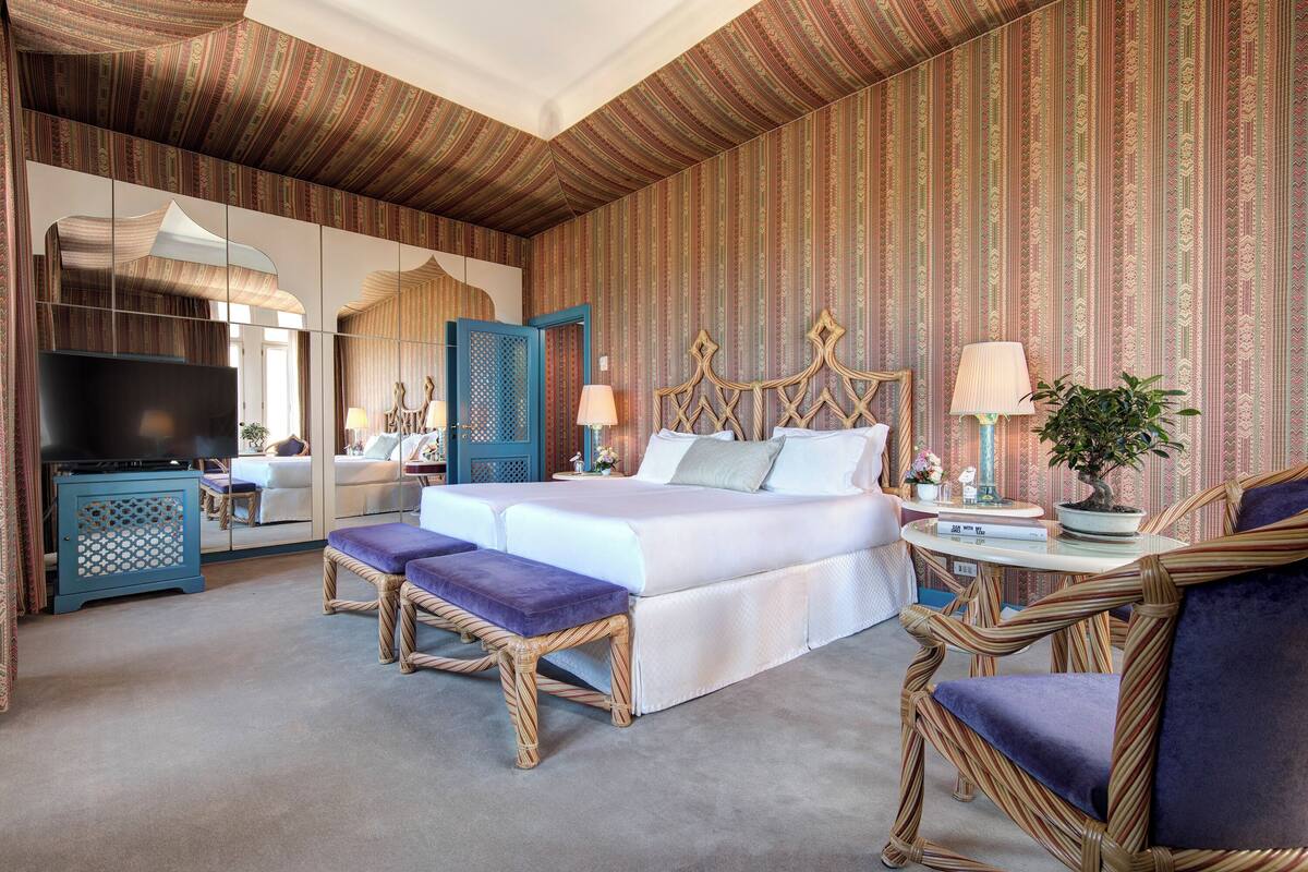 A hotel room with a large bed, two bedside tables, a television, and wicker furniture.