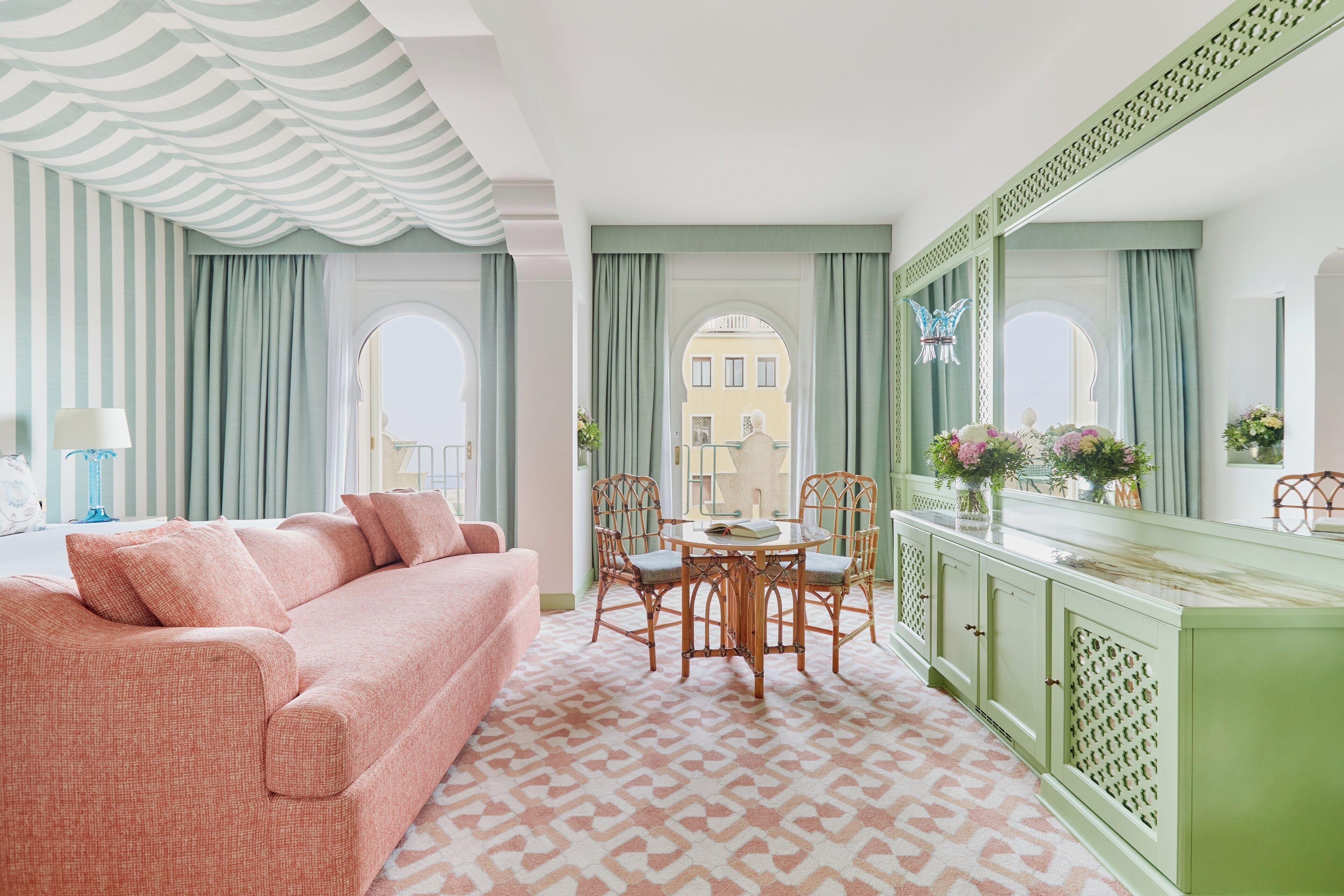 A room with a pink sofa, a green cabinet, and a dining table with chairs.