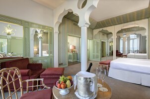Un'ampia stanza con un letto grande, un tavolo da pranzo con frutta e una bottiglia di champagne, e un'area salotto con poltrone e un divano.