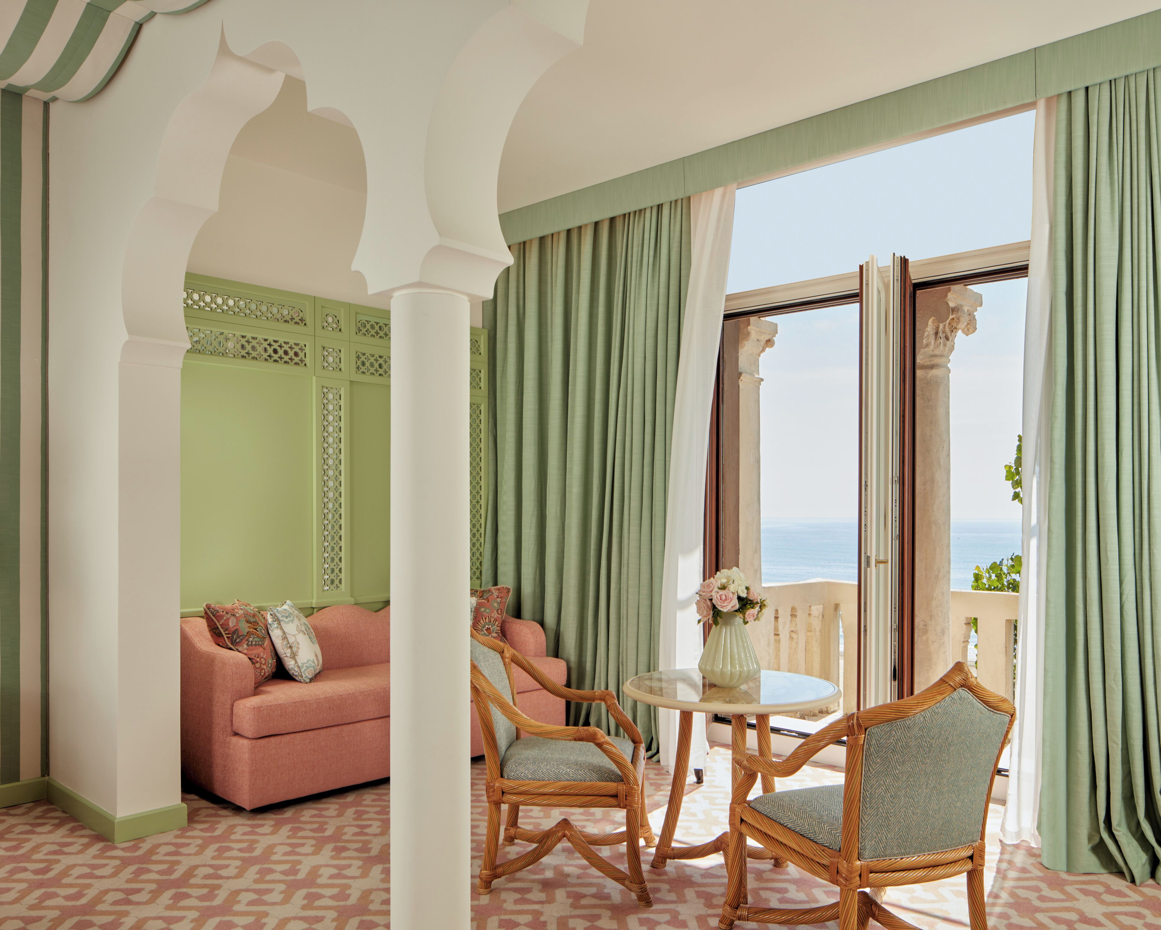 Una habitación con sofá, dos sillones, una mesa y vista al mar por una puerta abierta.