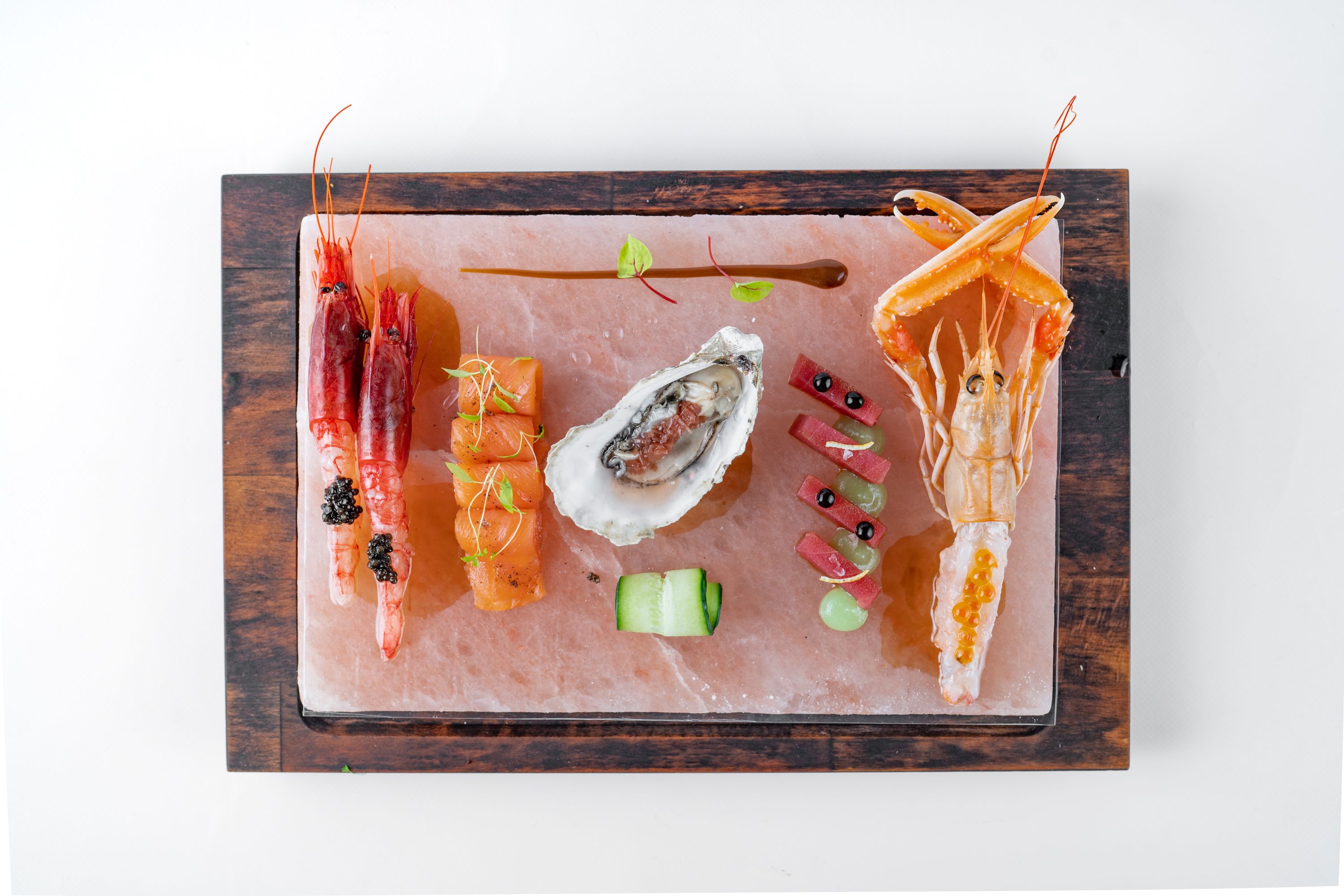 A seafood platter with shrimp, salmon, oysters, and garnishes on a marble board.