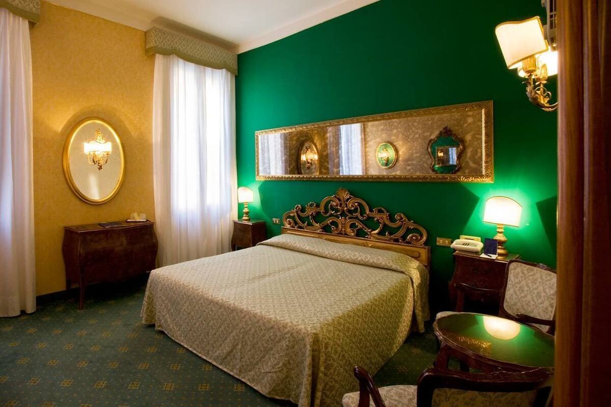 Une chambre d’hôtel avec un grand lit, un grand miroir rond, deux tables de chevet avec des lampes et un mur d’accent vert.
