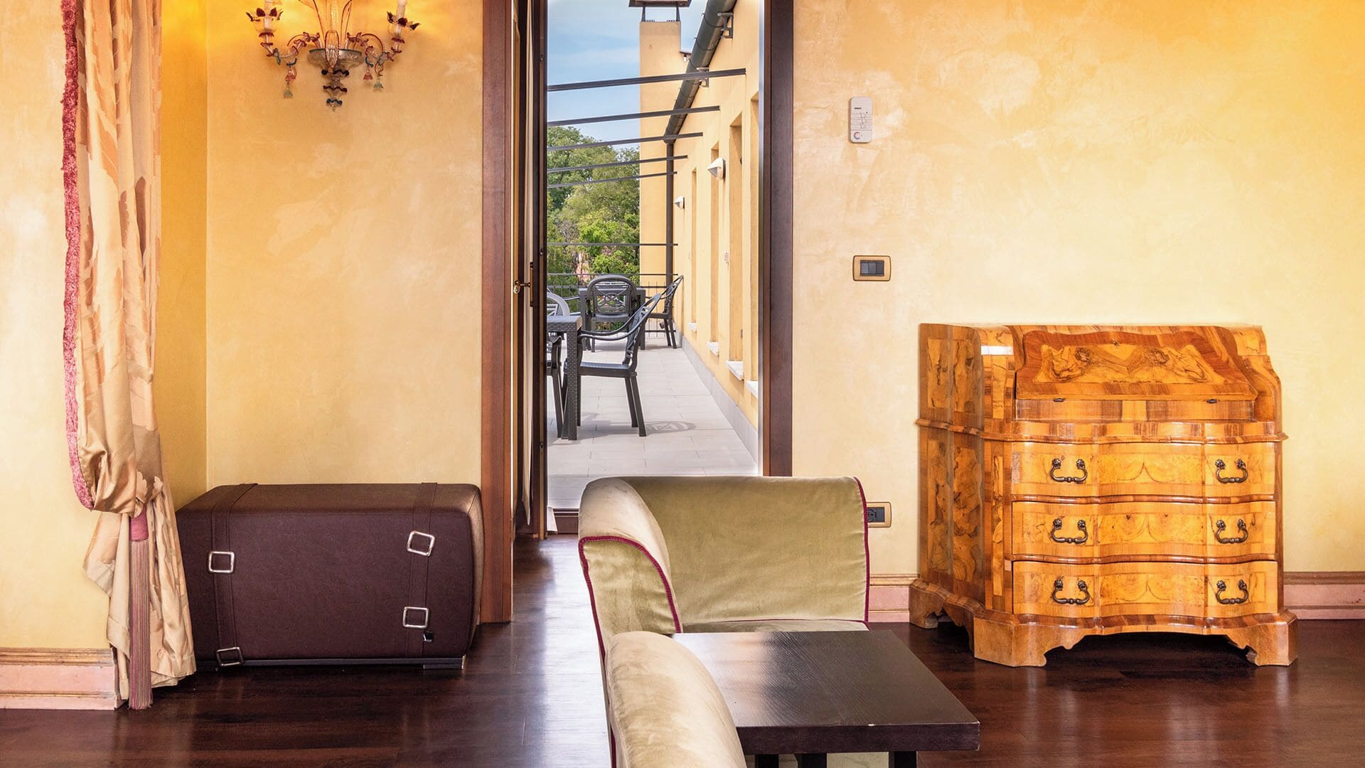 A room with a wooden chest of drawers, a bench, and a suitcase.