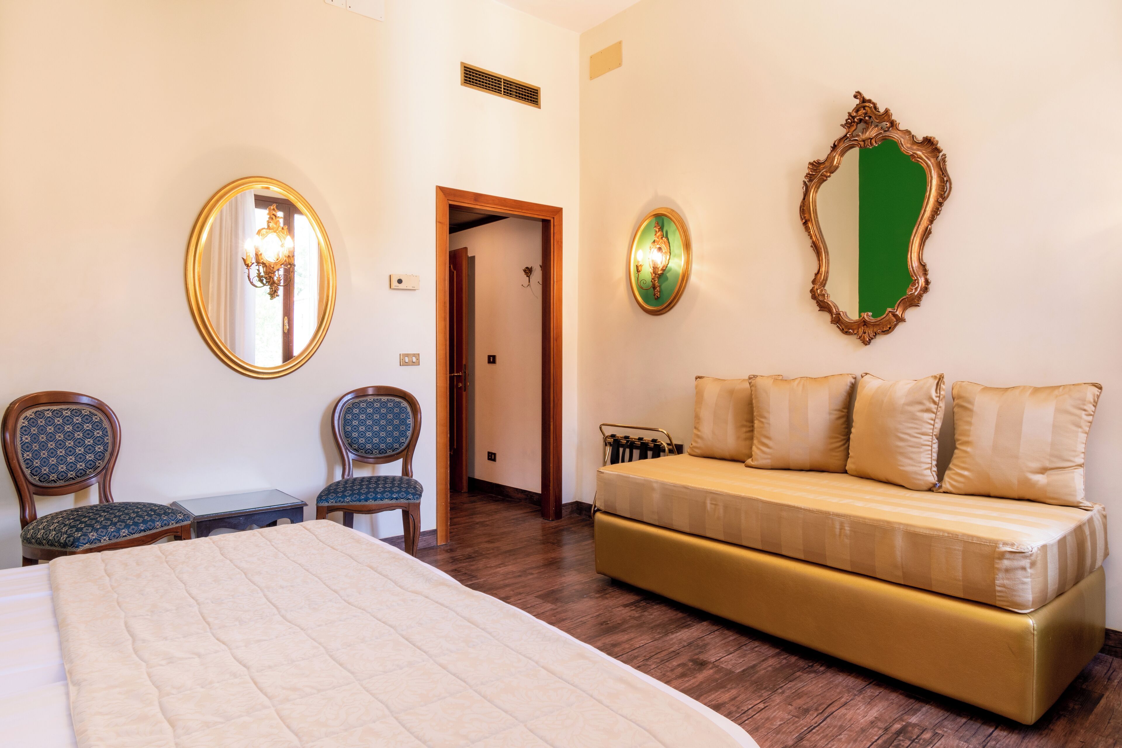 Une chambre d’hôtel comprenant un lit, deux chaises, un canapé et deux miroirs fixés au mur.
