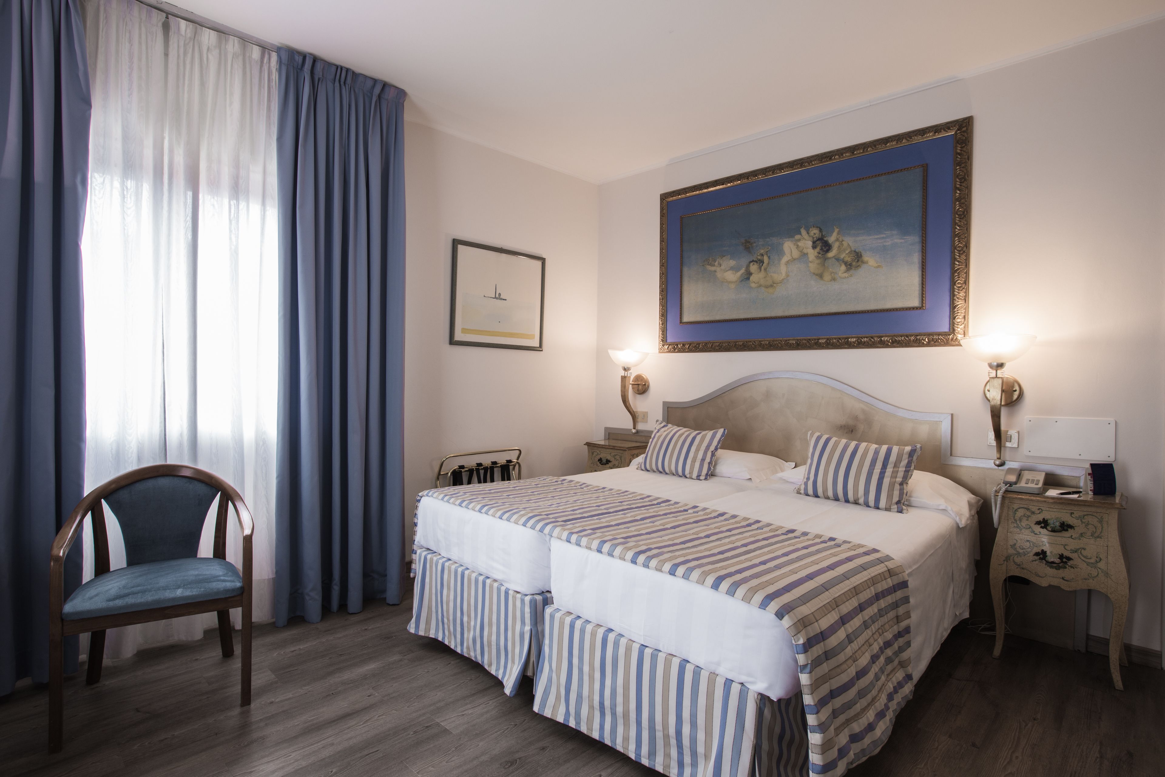 Ein Hotelzimmer mit einem großen Bett, einem Sessel, einem Nachttisch und einem Bild an der Wand.
