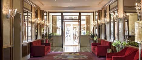 Un hall d’hôtel avec un sol à carreaux, des canapés rouges et des lustres.
