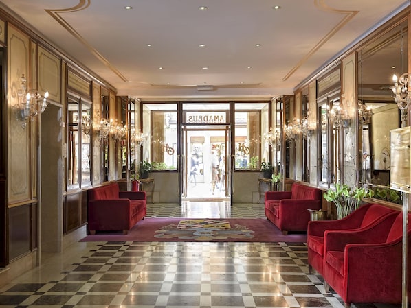 A hotel lobby with a checkered floor, red sofas, and chandeliers.