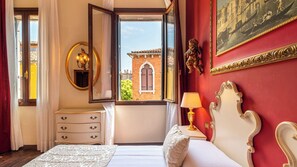A hotel room with a bed, a dresser, a mirror, a window with a view of a building, and a painting on the wall.