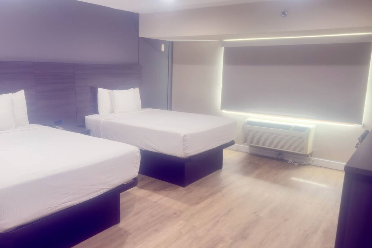 A hotel room with two beds, a built-in wardrobe, a bedside table, and a wall-mounted air conditioning unit.