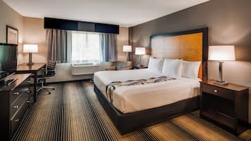 Een hotelkamer met een groot bed, een bureau met stoel, een televisie en een flatscreenmonitor.