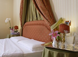 A hotel room with a bed, a bedside table with a lamp, a tray with glasses and a pitcher, and a potted orchid.