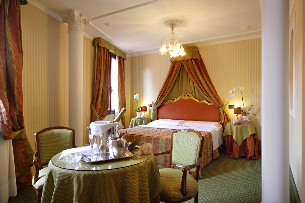 A hotel room with a bed, a sitting area with a table, and a chandelier.