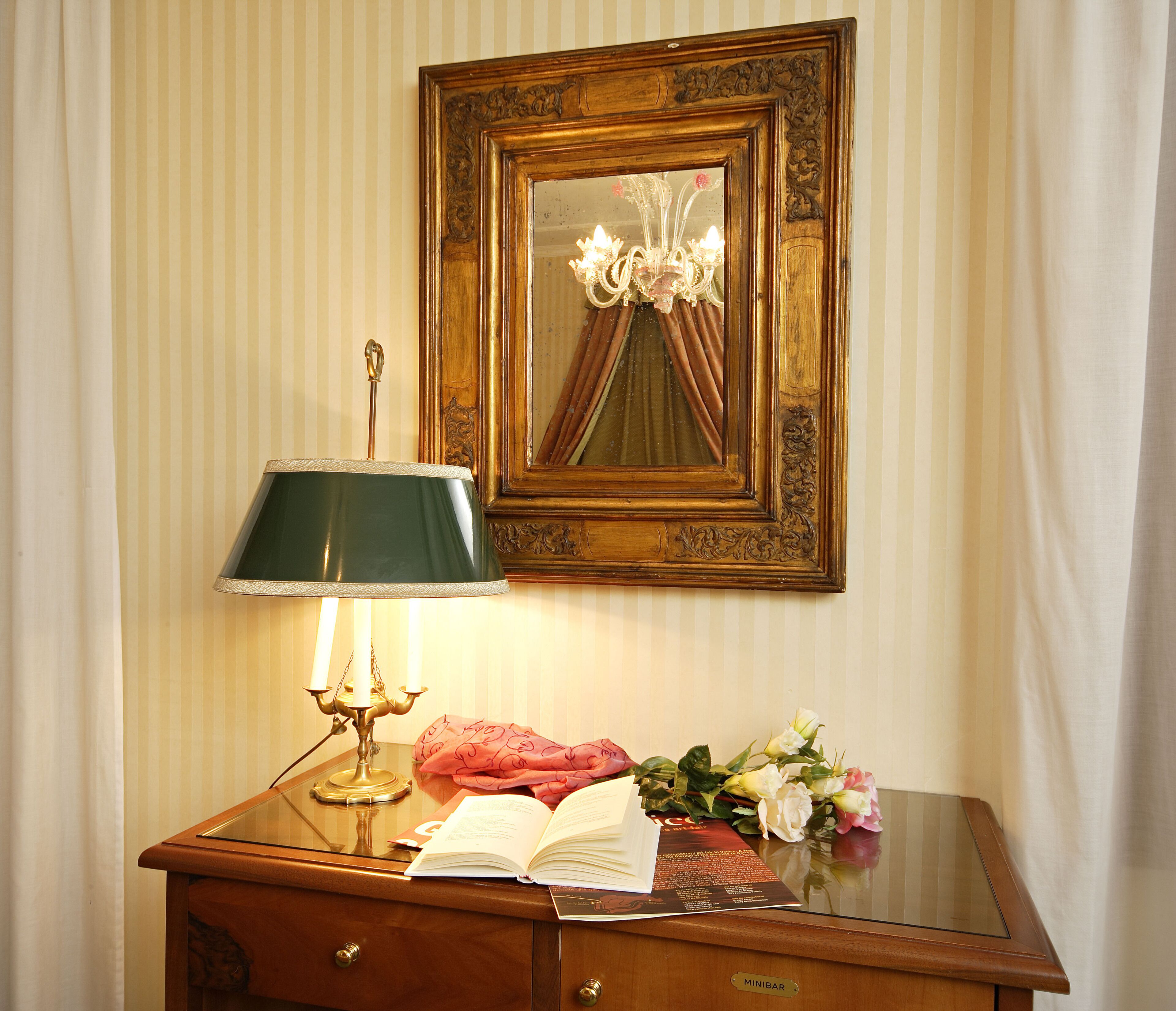 Un bureau en bois, une lampe verte, un livre ouvert et un bouquet de fleurs.