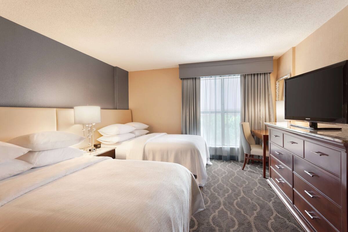 A hotel room with two beds, a TV, a desk, and a chair.