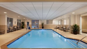 An indoor swimming pool with clear blue water, surrounded by lounge chairs and potted plants.