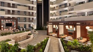 A multi-level hotel atrium with a central staircase, outdoor seating areas, and balconies with plants.