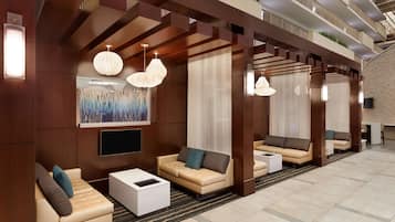 Un hall d’hôtel moderne doté d’espaces aménagés avec des sièges, d’un téléviseur à écran plat et d’un éclairage décoratif.