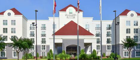 Un hotel con un llamativo letrero de 'Embassy Suites', varias banderas y un césped delantero bien cuidado.
