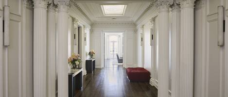A grand hallway with ornate white columns, a skylight, and a red upholstered bench.
