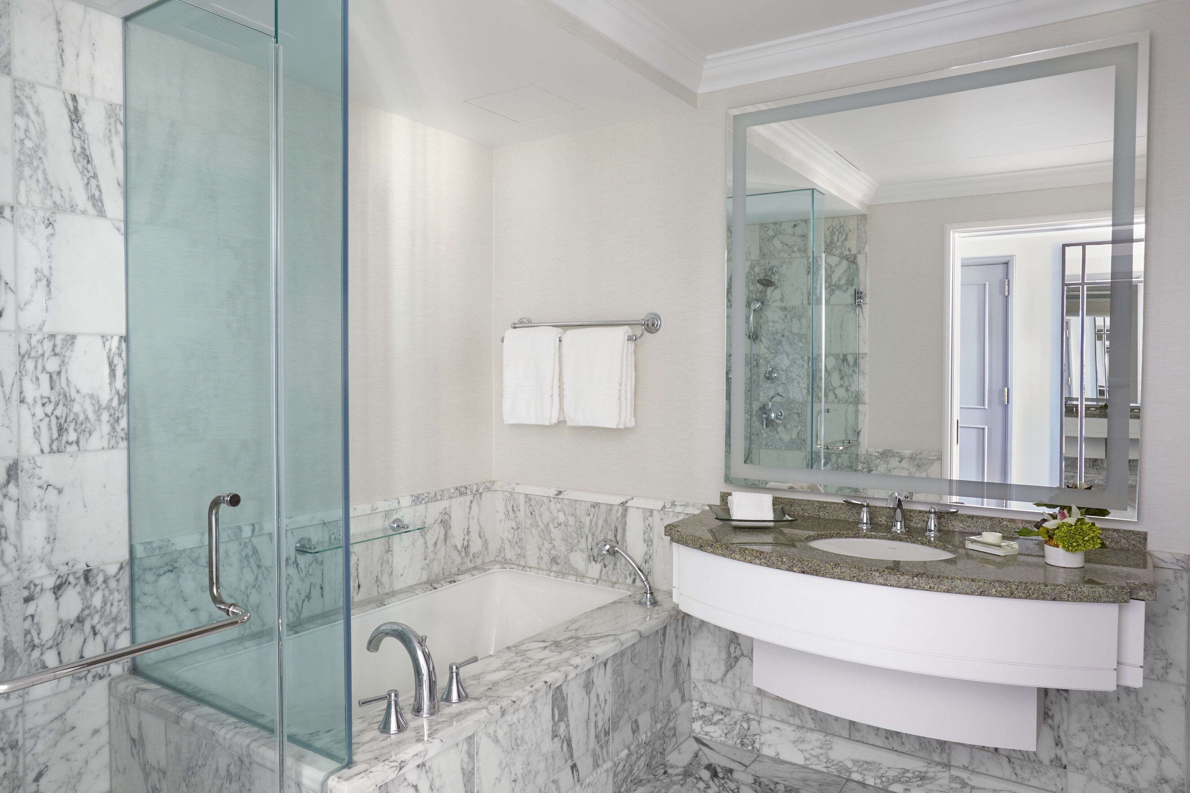 A bathroom with a glass-enclosed shower, a marble bathtub, a sink with a granite countertop, and a large mirror.