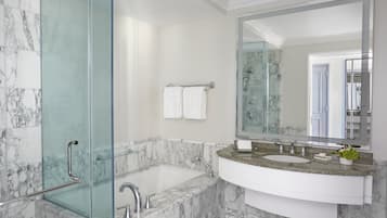 A bathroom with a glass-enclosed shower, a marble bathtub, a sink with a granite countertop, and a large mirror.