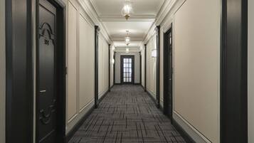 A long, narrow hallway with a patterned carpet, black doors, and a chandelier.